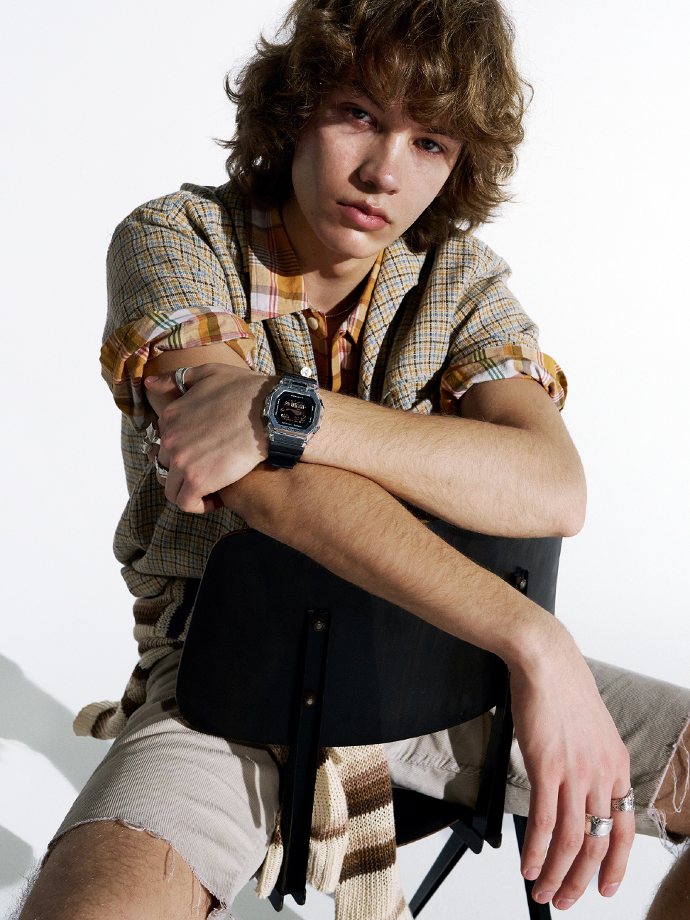 年轻男子佩戴金属 G-SHOCK，双臂放在椅子上摆姿势。