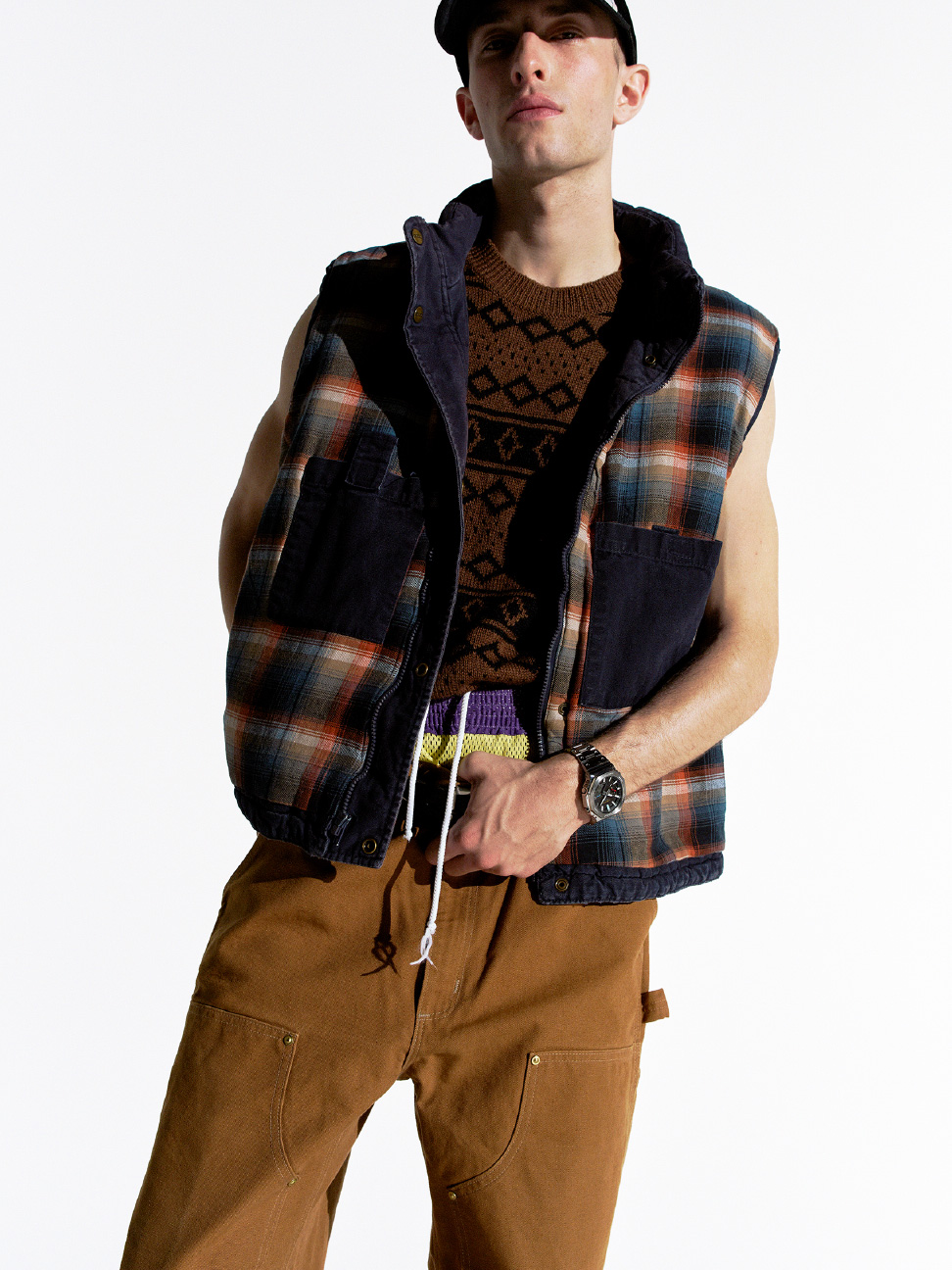 身穿黑色 G-SHOCK 和格纹背心的人，以休闲姿势站立。