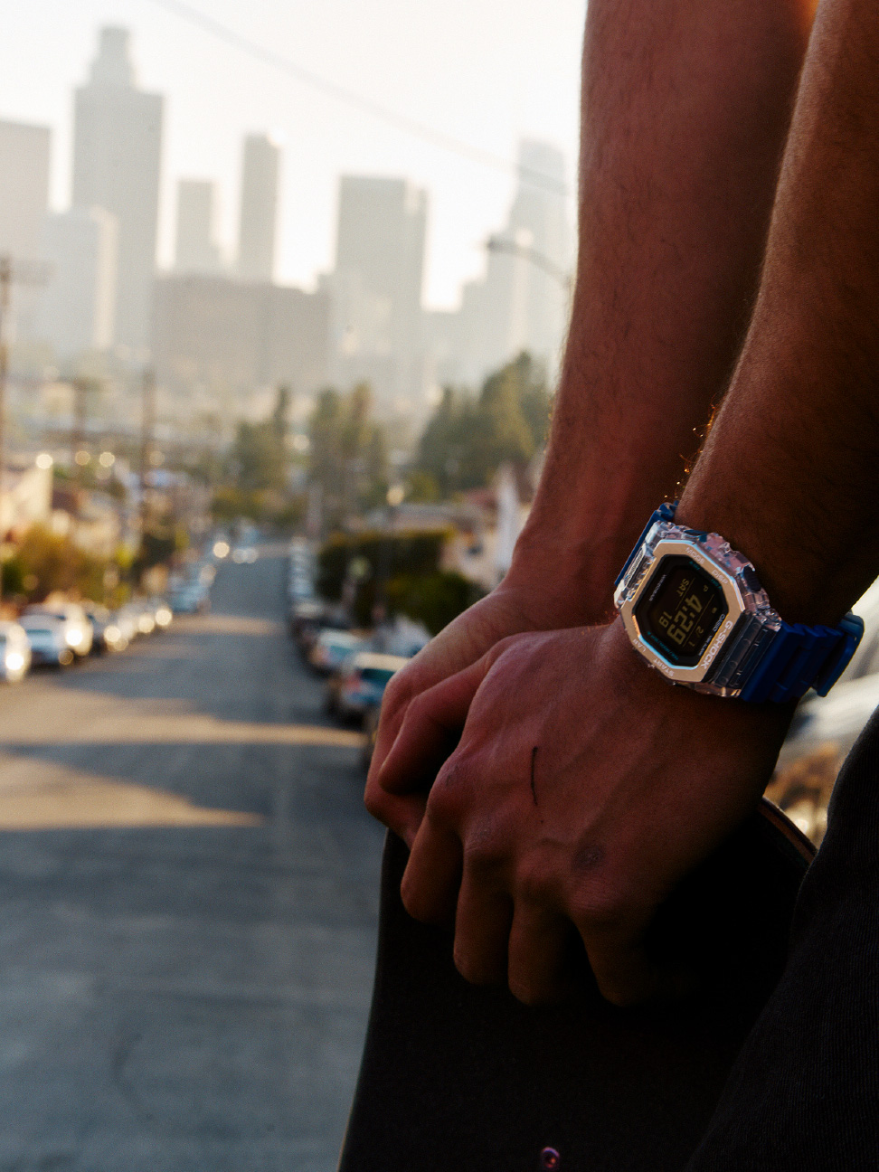 身穿蓝色 G-SHOCK 的人手持滑板，俯瞰城市。