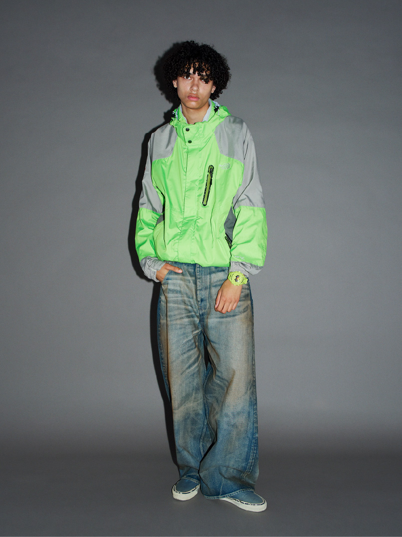 身穿霓虹色 G-SHOCK 和绿色夹克的人，以休闲姿势站立。