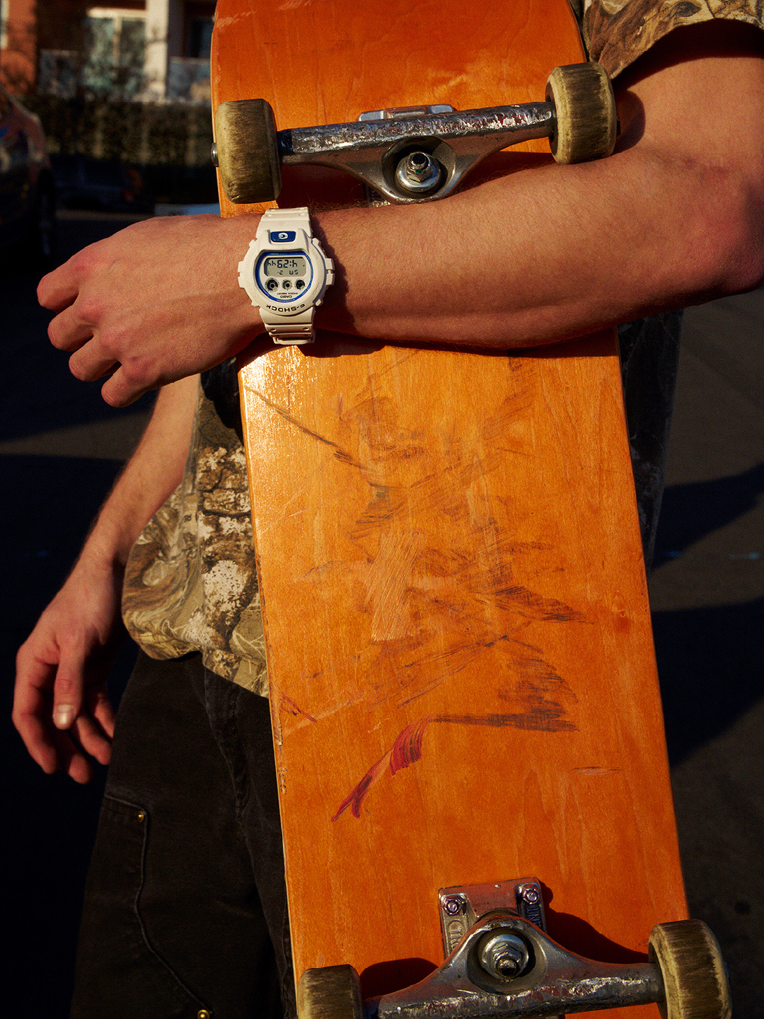 身穿白色 G-SHOCK 的人手持滑板。