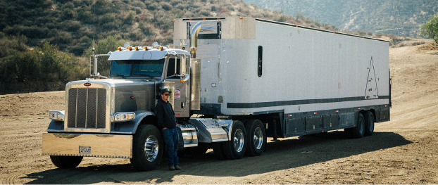 一张半挂卡车停在宽阔的未铺设路面公路上的照片。